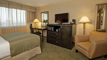 Habitación de hotel con cama, escritorio con silla, televisor, minibar y lámpara.