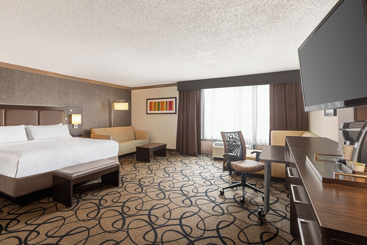 A hotel room with a large bed, a sofa, a desk, and a TV.