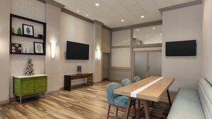 A modern conference room with a wooden floor, a green cabinet, a white table with blue chairs, and two flat-screen TVs mounted on the walls.