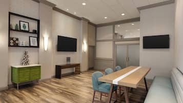 A modern conference room with a wooden floor, a green cabinet, a white table with blue chairs, and two flat-screen TVs mounted on the walls.