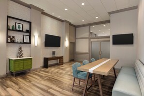 A modern conference room with a wooden floor, a green cabinet, a white table with blue chairs, and two flat-screen TVs mounted on the walls. - Holiday Inn Boston - Cambridge Area by IHG (Somerville)