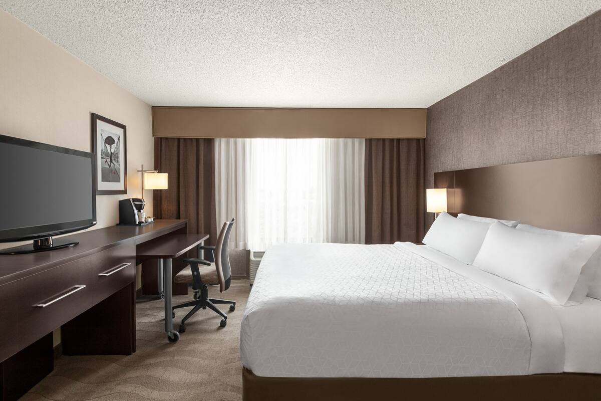 A hotel room with a large bed, a desk with a chair, a television, and two lamps.