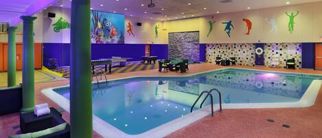 An indoor swimming pool with a checkered floor, poolside chairs, and a projection screen displaying animated characters.