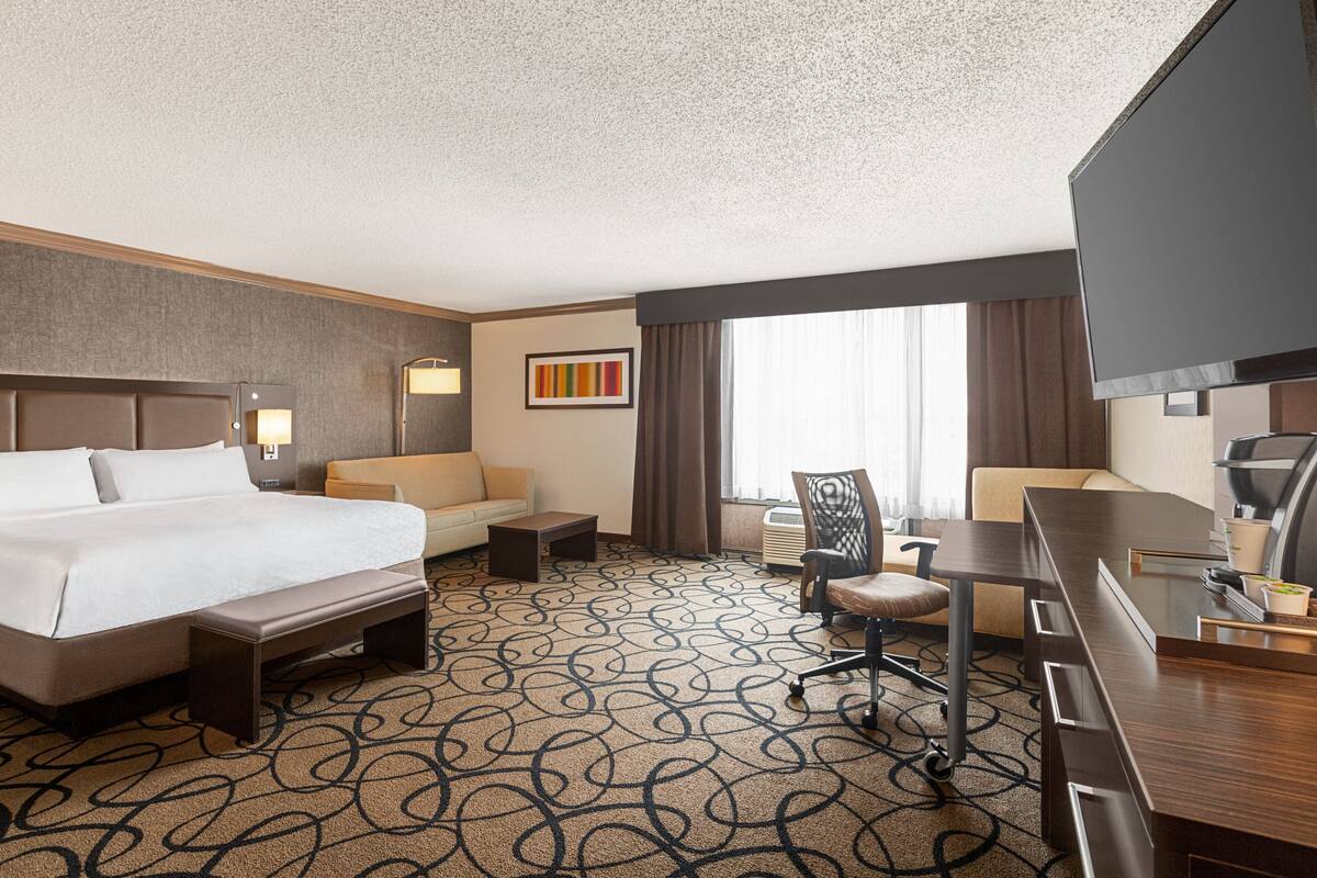 A hotel room with a large bed, a sofa, a desk, and a TV.