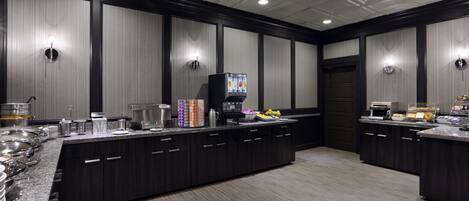 A buffet setup with a coffee machine, food containers, and a variety of food items.