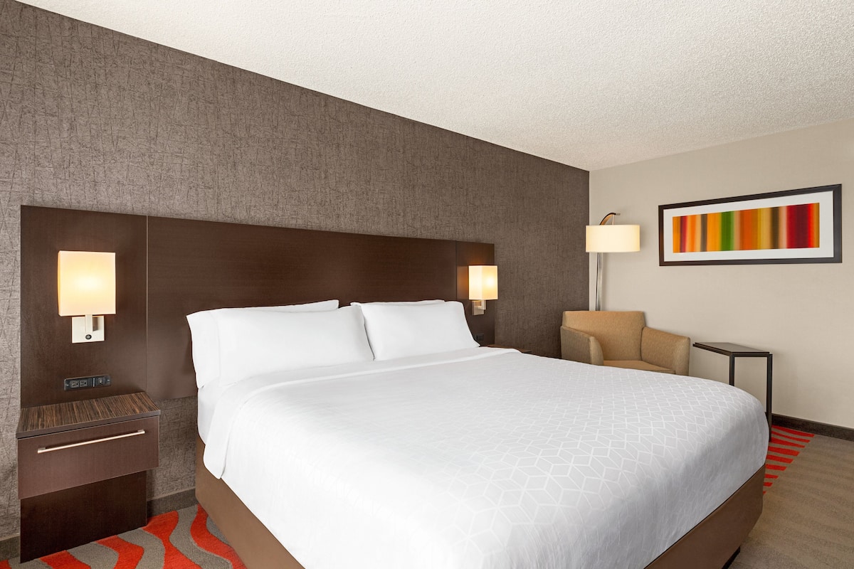 A hotel room with a large bed, two bedside tables, a nightstand, a lamp, and a framed picture on the wall.