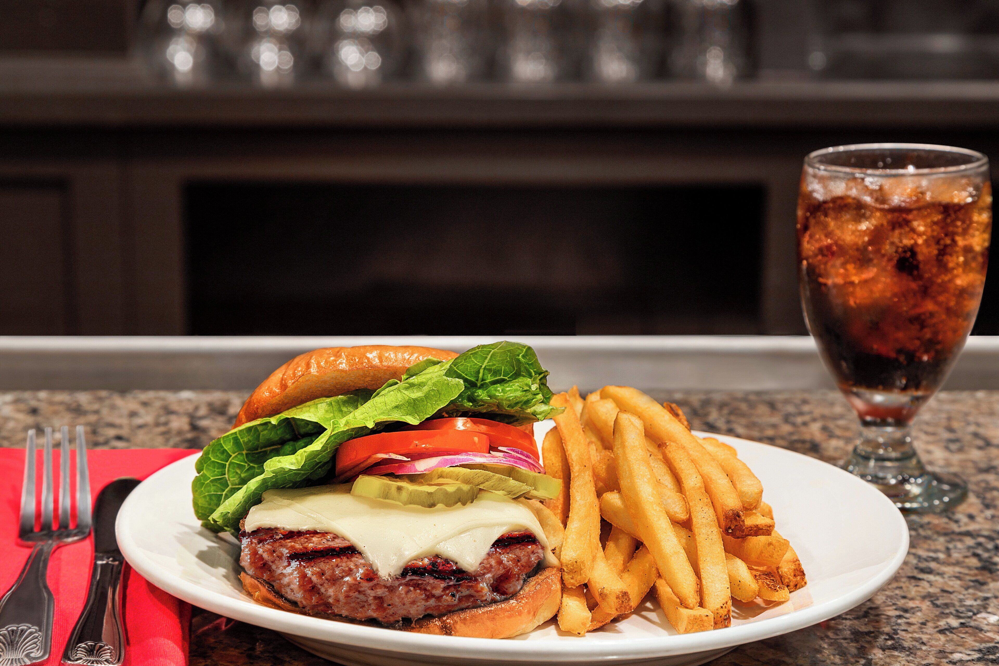 Un plato con una hamburguesa, papas fritas y un vaso de refresco.