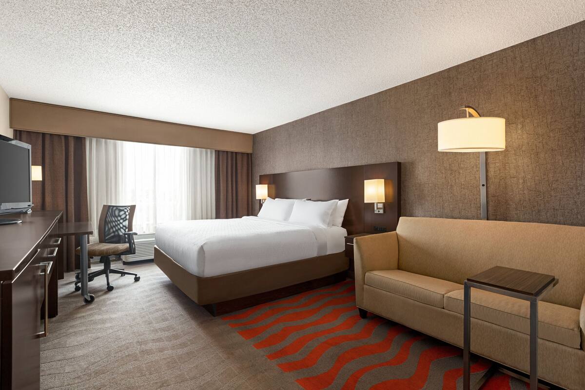 A hotel room with a bed, a sofa, a desk, and a TV.