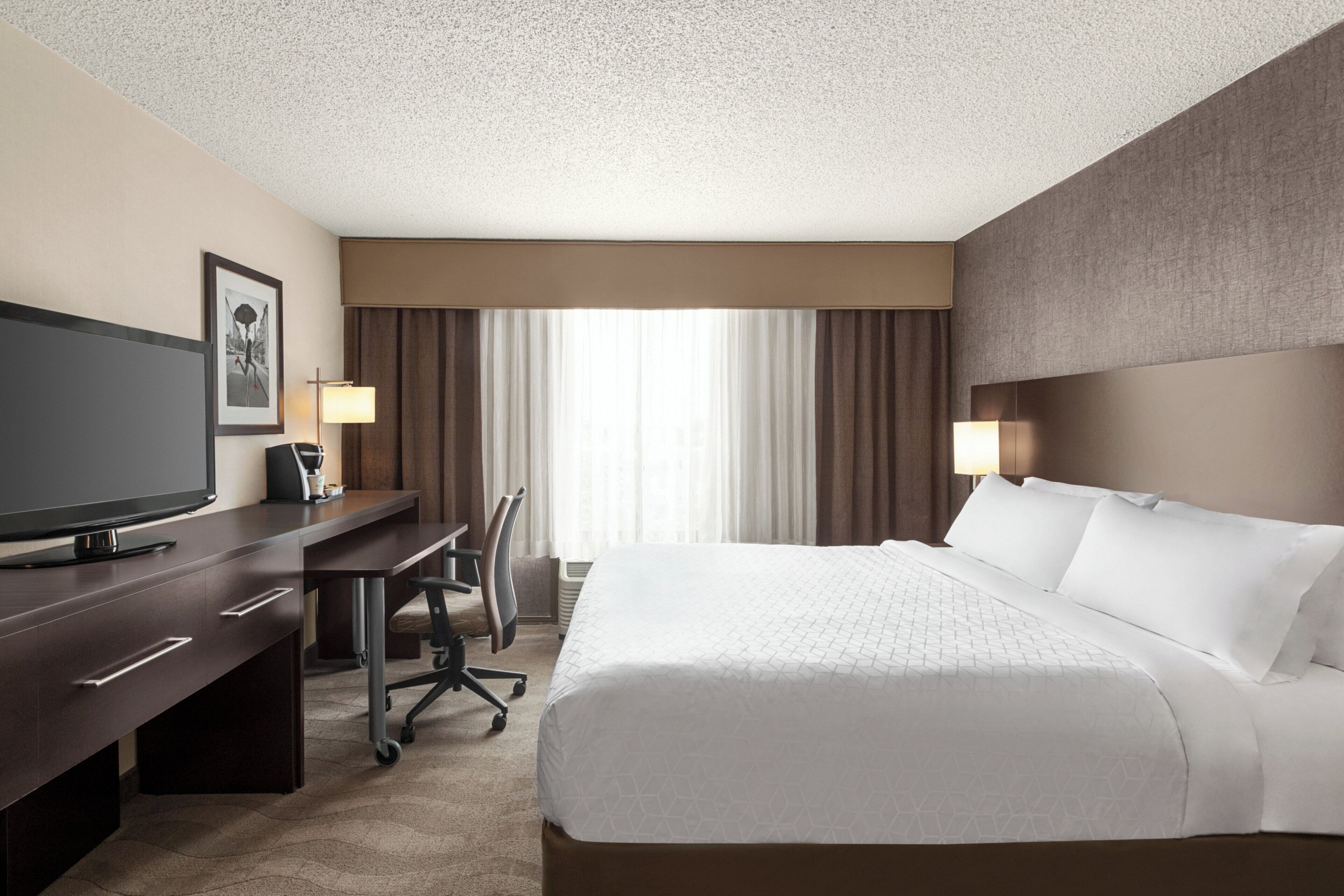 A hotel room with a bed, desk, chair, television, and two lamps.
