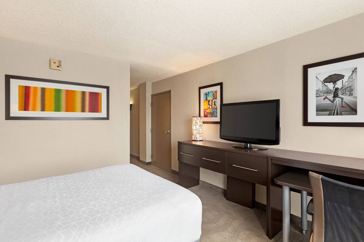 A hotel room with a bed, a desk with a television, and artwork on the walls.