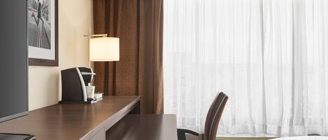 Ett hotellrum med ett skrivbord i trä, en stol, en tv, en lampa och en säng med ett geometriskt mönster på sängöverkastet.