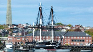A tall ship docked at a harbor with a prominent monument in the background.