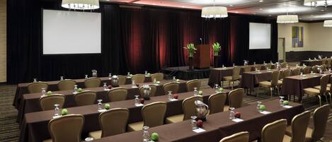A conference room with tables set for a meeting, a stage with a podium, and a large screen.