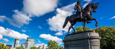 Una estatua de una figura a caballo sobre un pedestal, con la palabra “WASHINGTON” grabada, frente a un cielo azul despejado y un paisaje urbano.