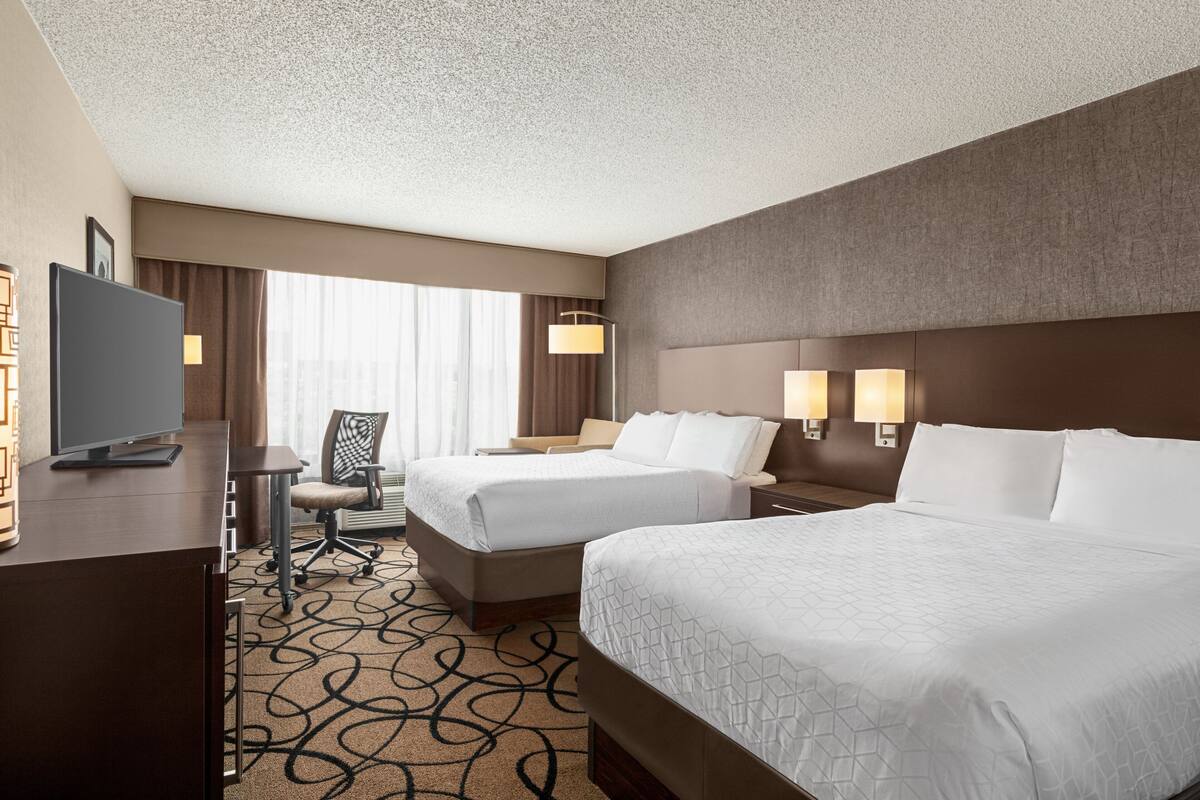 A hotel room with two beds, a desk, a chair, a TV, and a window with curtains.