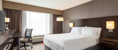 Habitación de hotel con una cama grande, un escritorio con silla, un televisor y dos lámparas de noche.