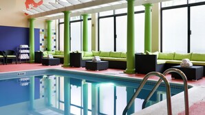 A pool area with green pillars, a sofa, and a lounge chair.