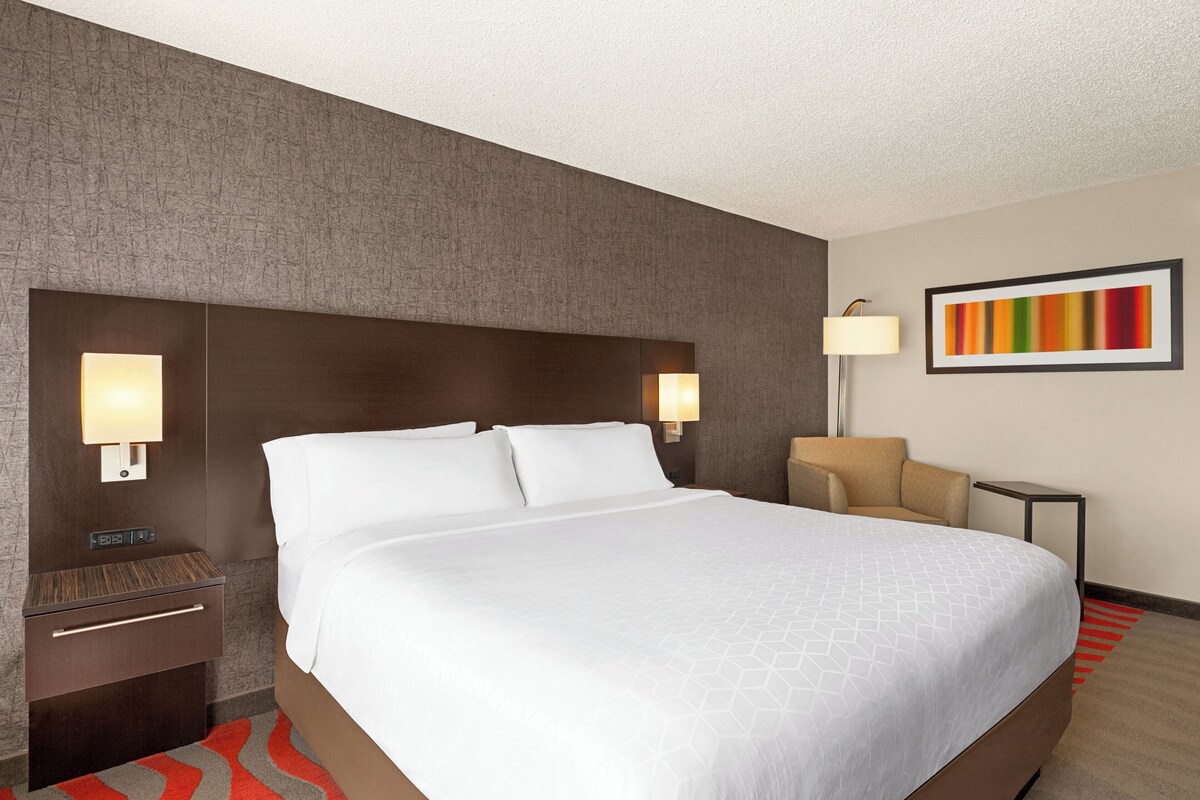 A hotel room with a large bed, two bedside tables, a nightstand, a lamp, and a framed picture on the wall.
