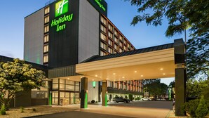 A Holiday Inn hotel with a modern design, featuring a prominent sign, a covered entrance, and a parking area.