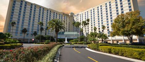 A large hotel with a central plaza, palm trees, and a clear sky.