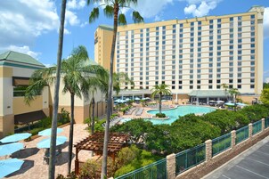 A hotel with a large pool, outdoor seating, and palm trees.