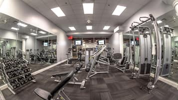 A gym with various exercise equipment, mirrors, and a rack of dumbbells.
