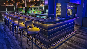 A bar area with a long counter, multiple stools, and shelves stocked with bottles. - Rosen Plaza on International Drive (Orlando)