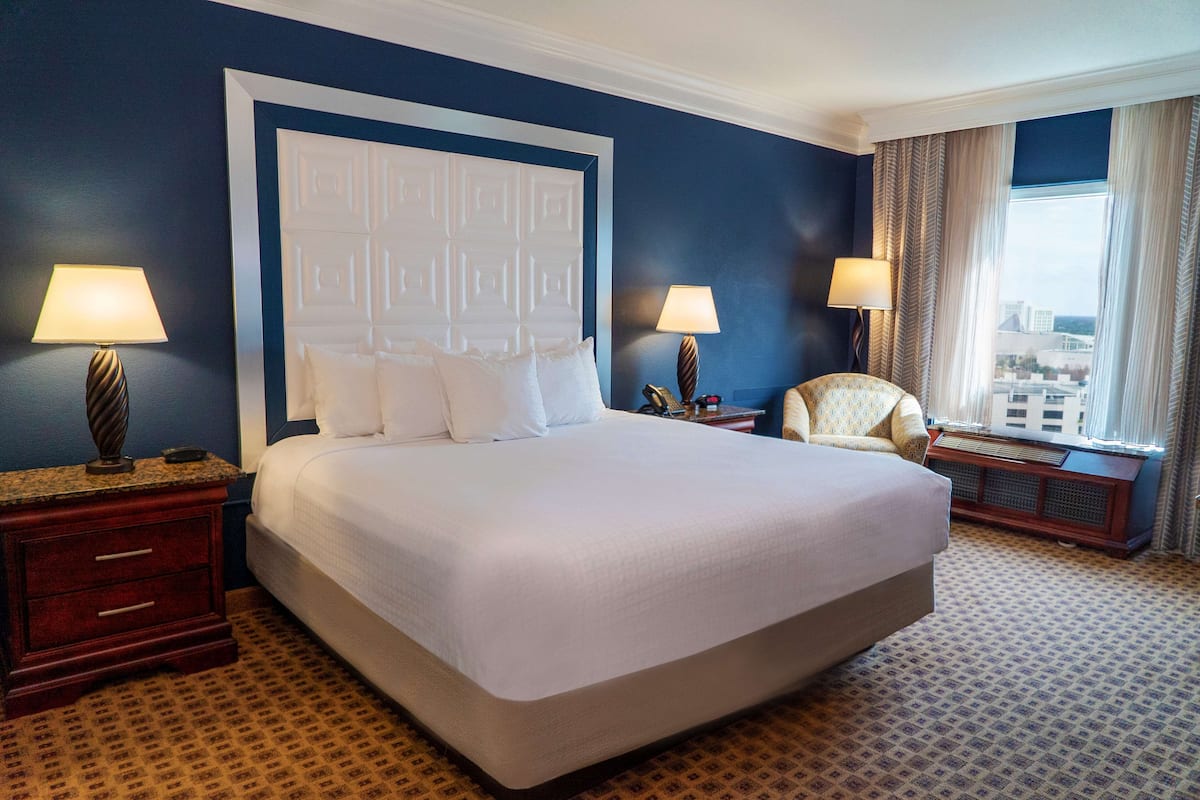 Une chambre d’hôtel avec un grand lit, deux tables de chevet, une chaise et une vue sur la ville par la fenêtre.