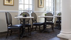 A dining area with four tables and chairs, each with a small plant. There are two framed artworks on the walls. - The Willows Hotel (Chicago)