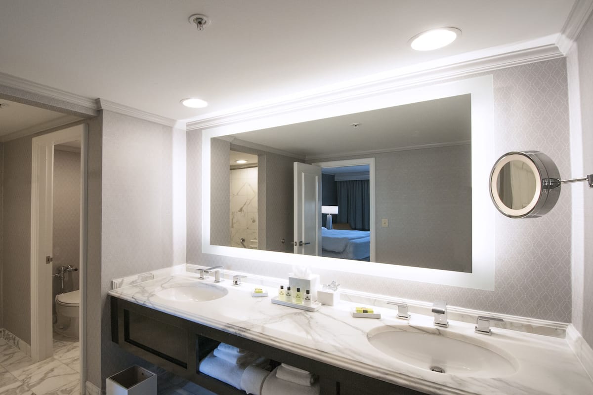 Un baño moderno con un espejo grande, dos lavamanos y una ducha.