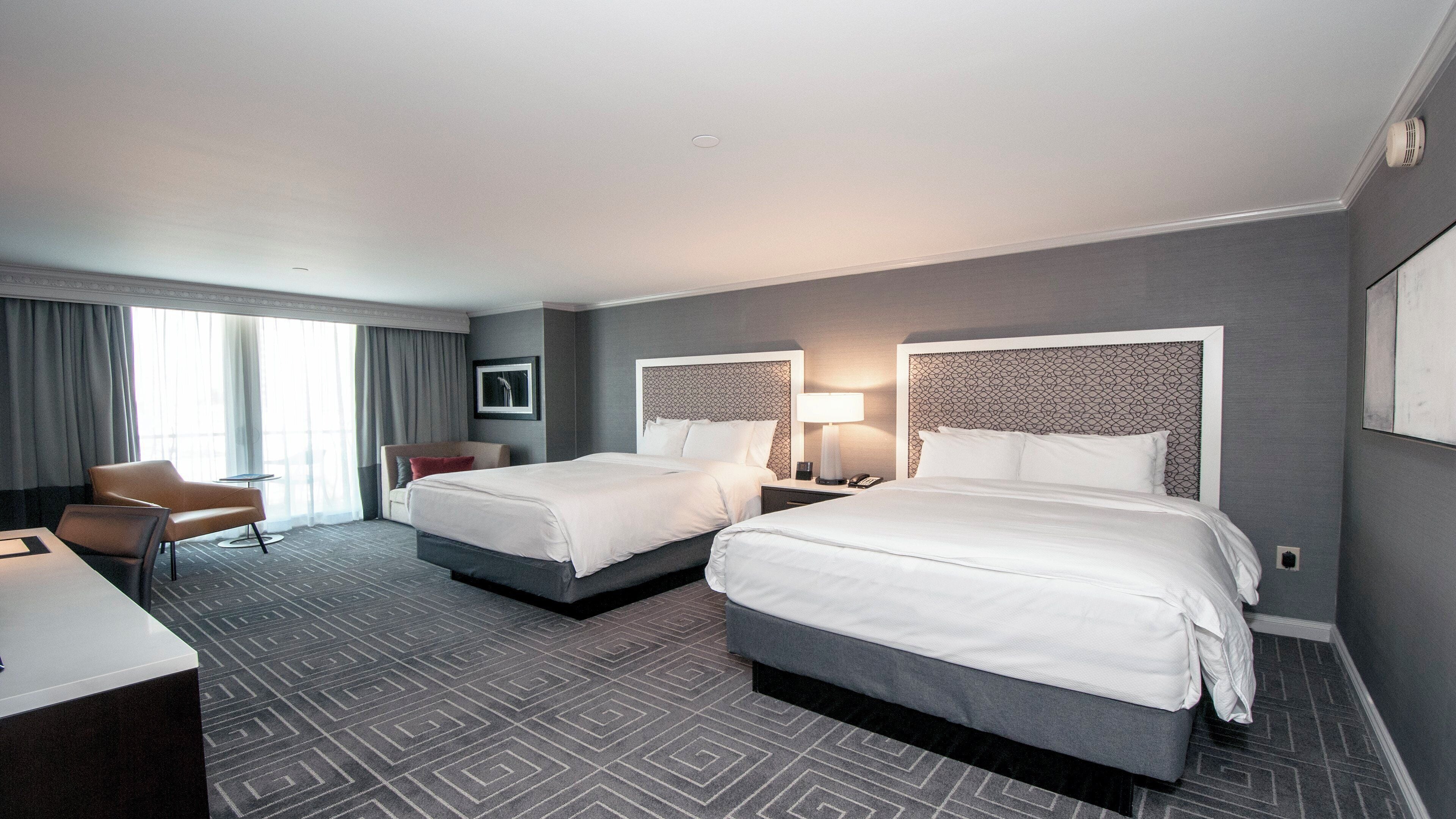 Ein Hotelzimmer mit zwei Betten, einem Schreibtisch, einem Stuhl und einem fenster mit Vorhängen.