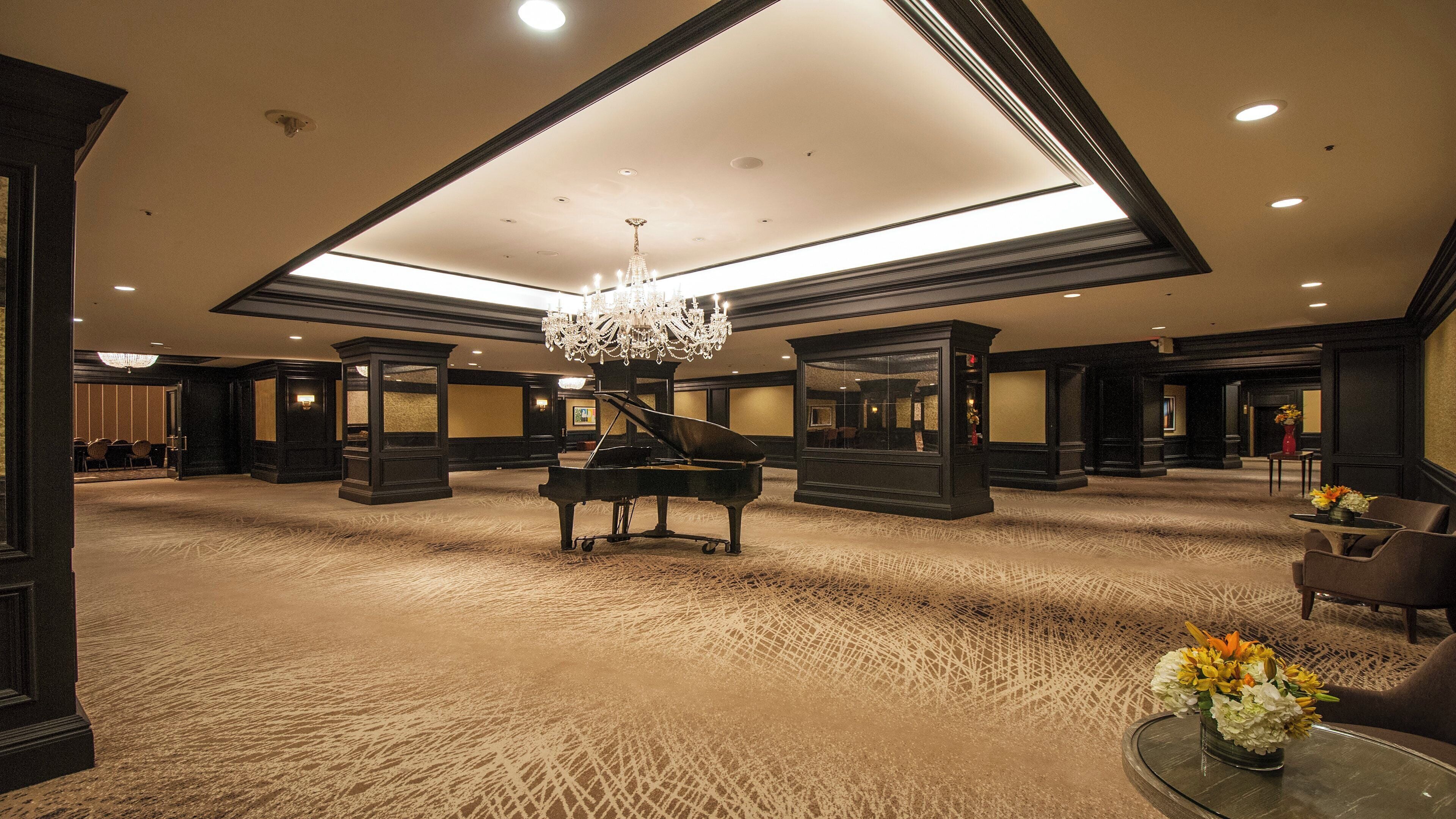 A grand lobby with a grand piano, a chandelier, and a carpeted floor.