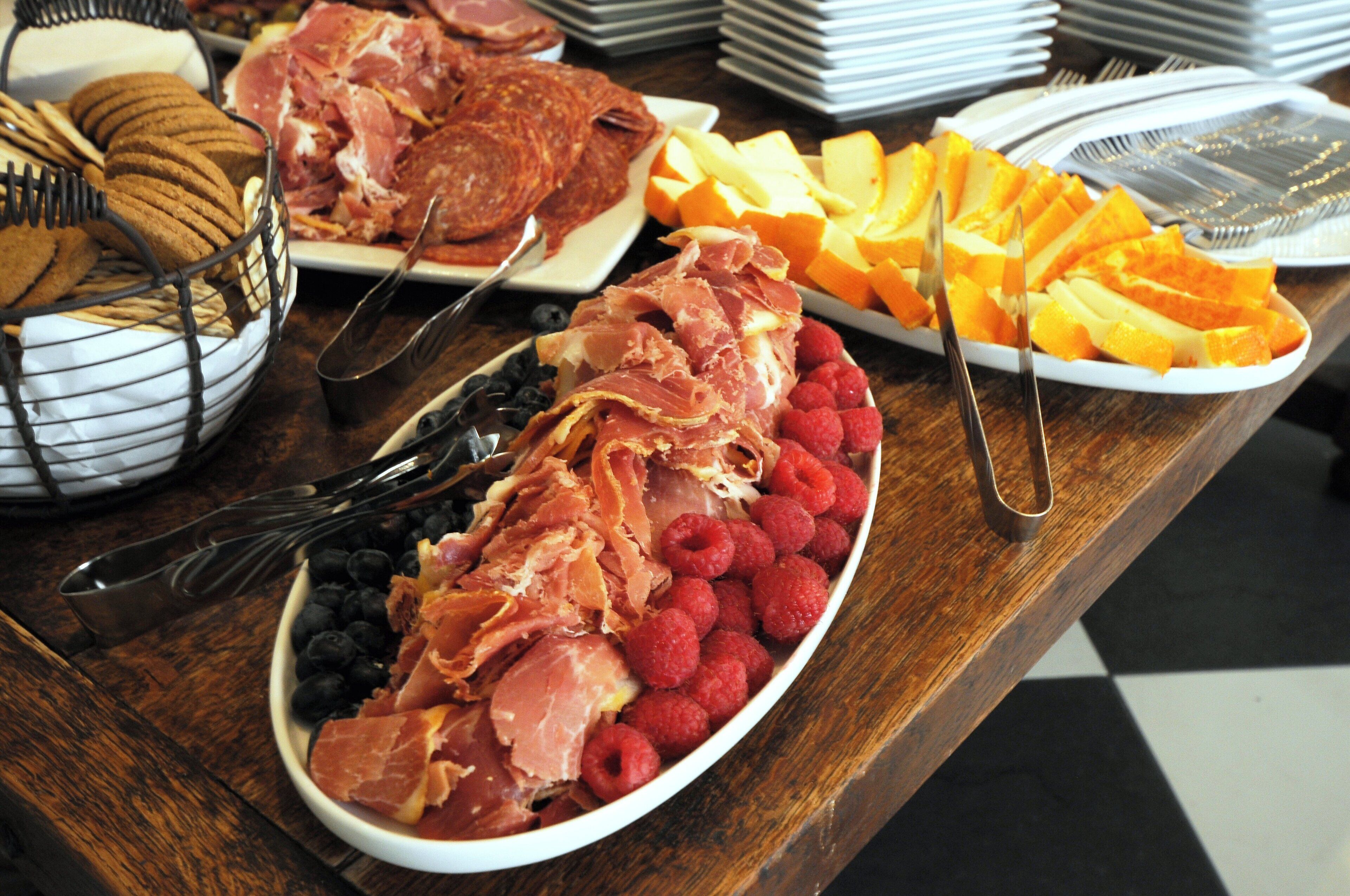Una mesa de buffet con diversos alimentos, incluyendo jamón, queso, frambuesas y galletas.