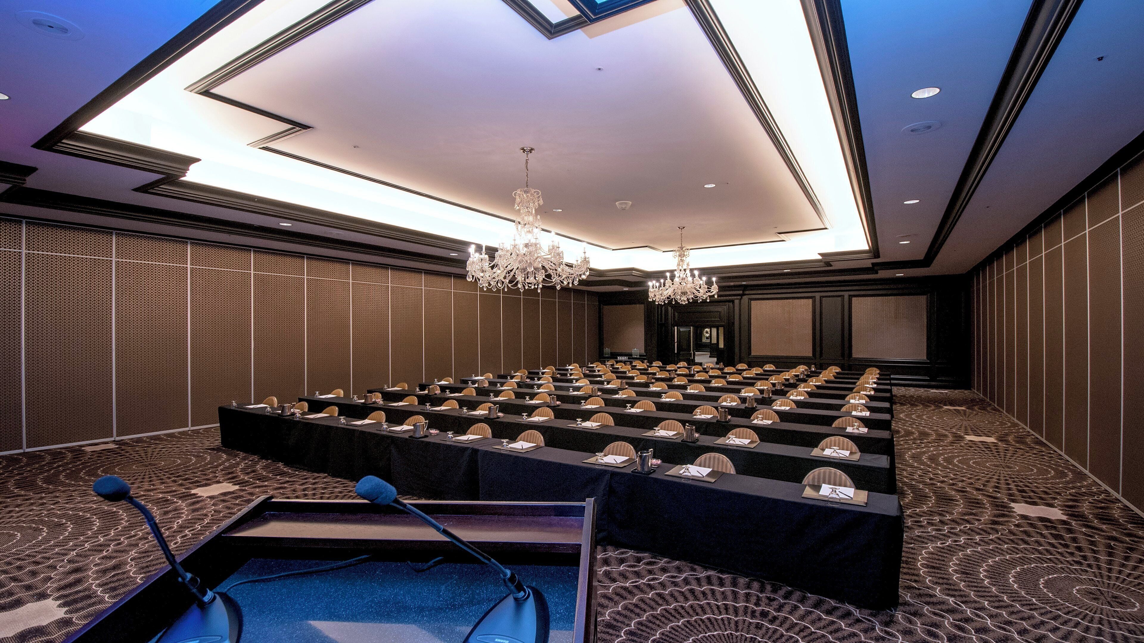 A conference room with rows of tables and chairs, a large chandelier, and a patterned carpet.