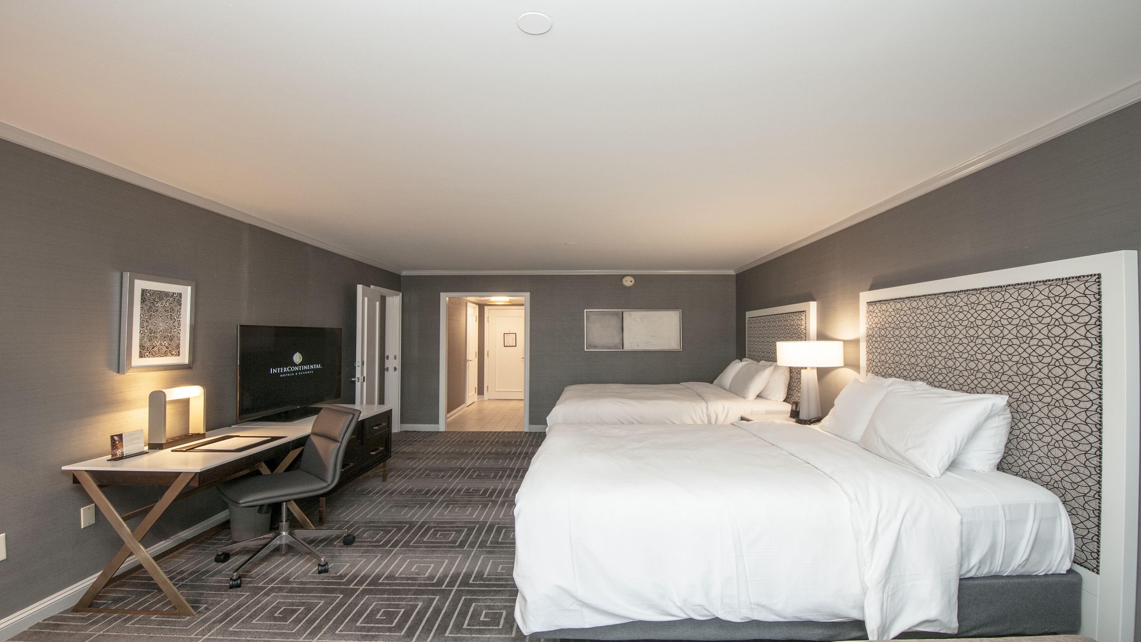 Habitación de hotel con cama, escritorio, silla, televisor y una puerta que da a otra habitación.