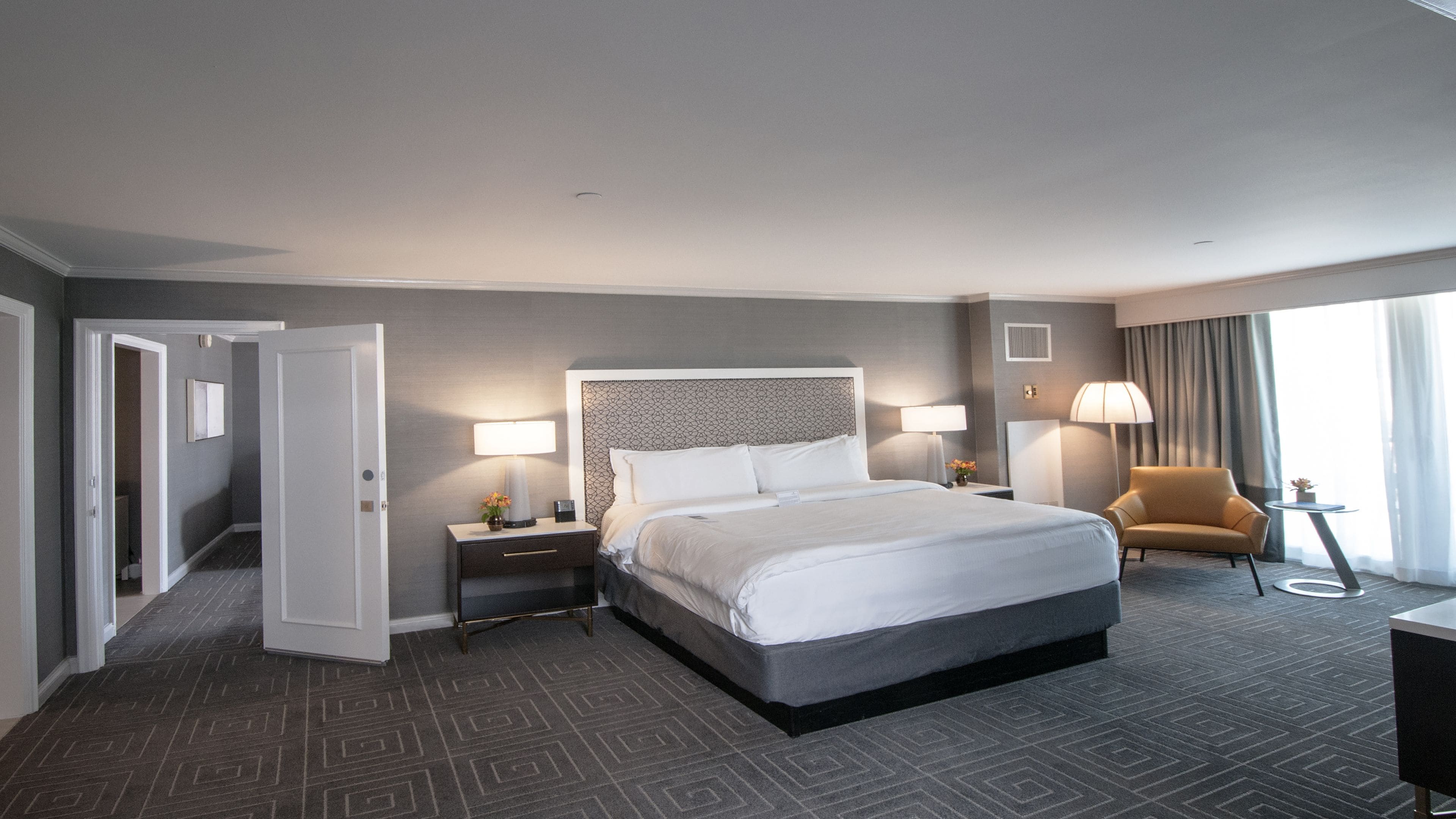 Habitación de hotel con una cama grande, mesitas de noche, una silla y vistas al exterior.