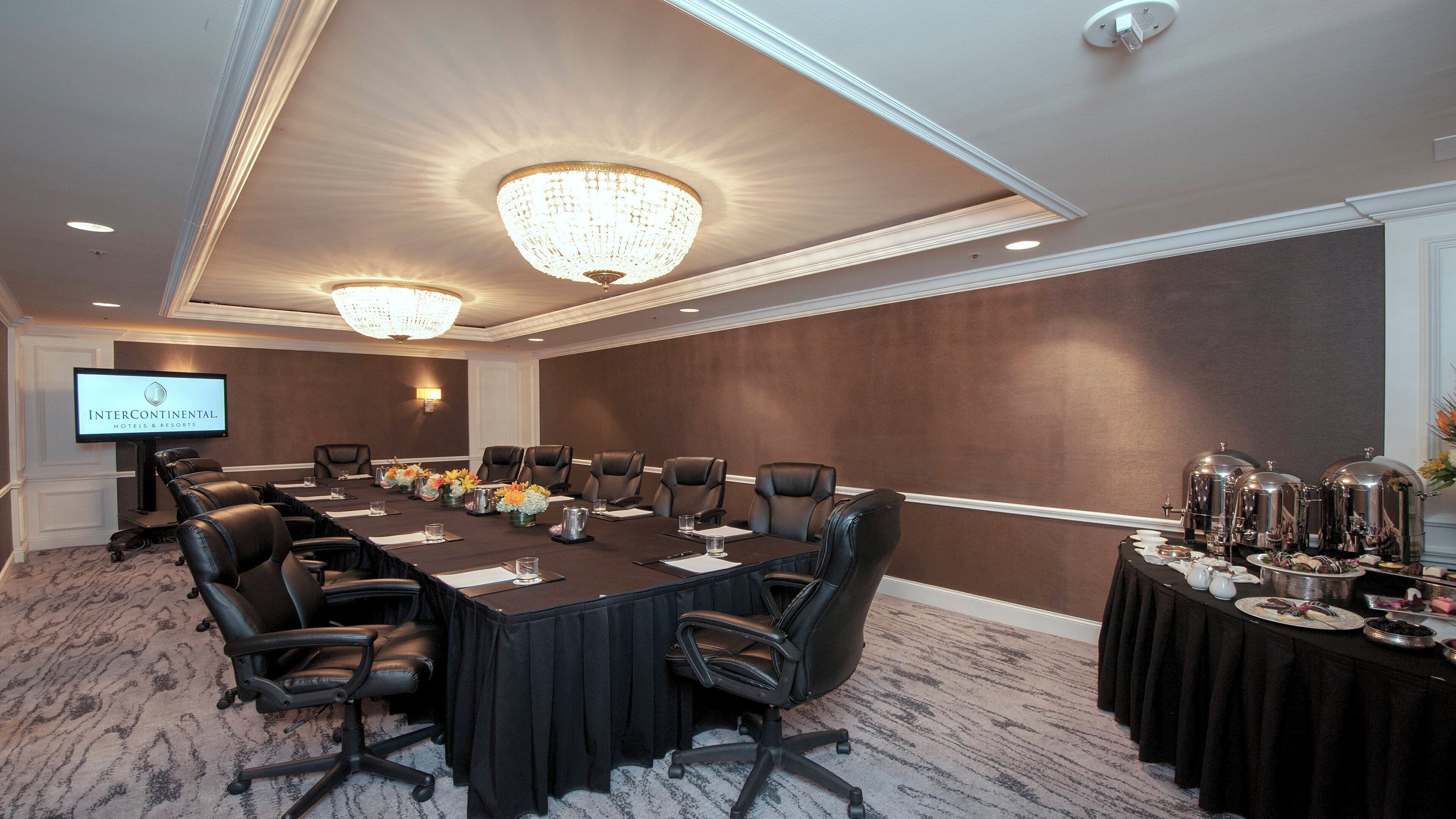 A conference room with a long table, chairs, a television screen, and a buffet table with food and drinks.