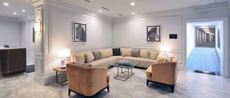 Una sala de estar moderna con un sofá seccional color beige, dos sillones, una mesa de centro de vidrio y un escritorio con una lámpara.