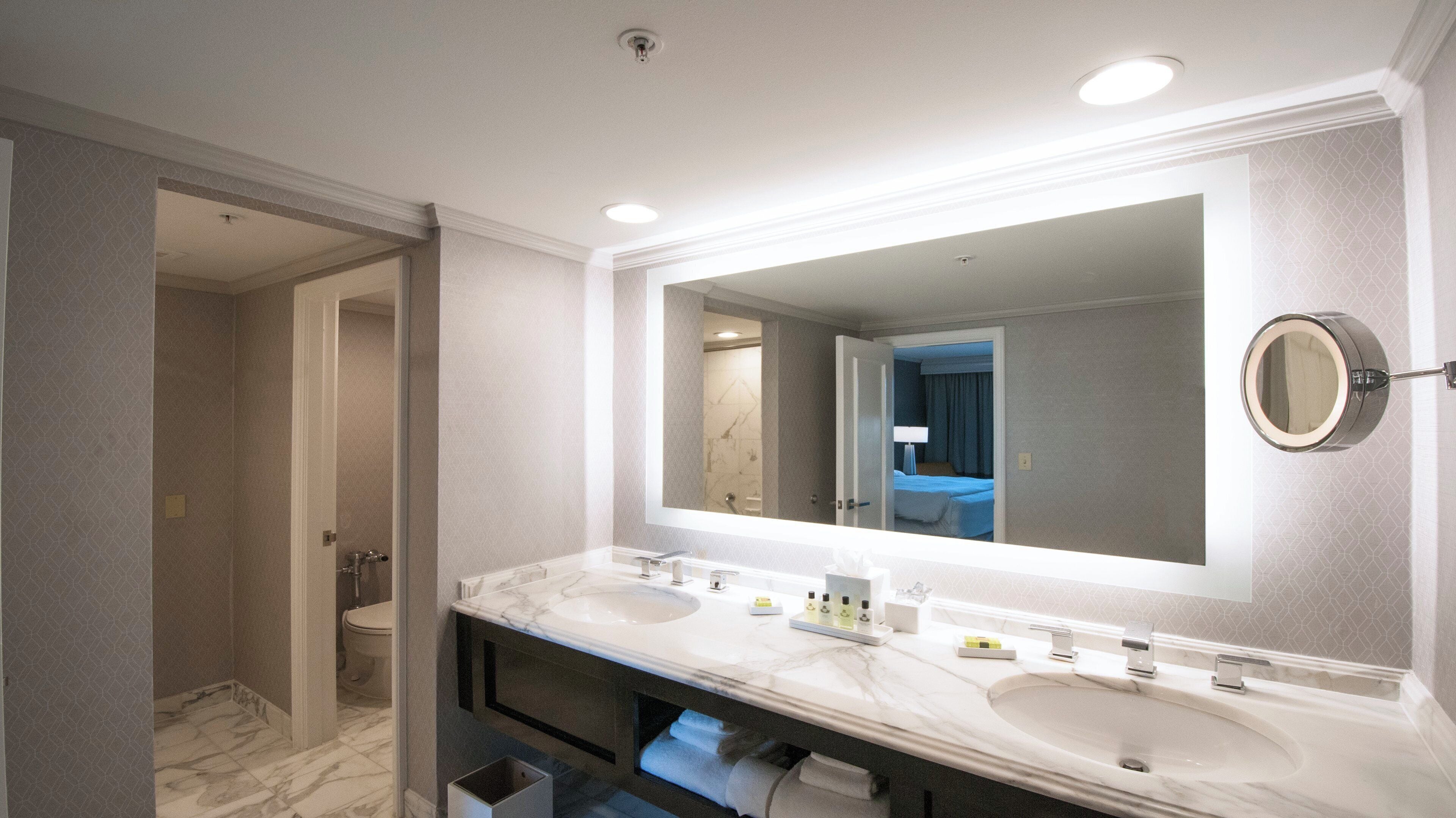 Une salle de bain moderne avec un grand miroir, deux lavabos, une douche et des toilettes.