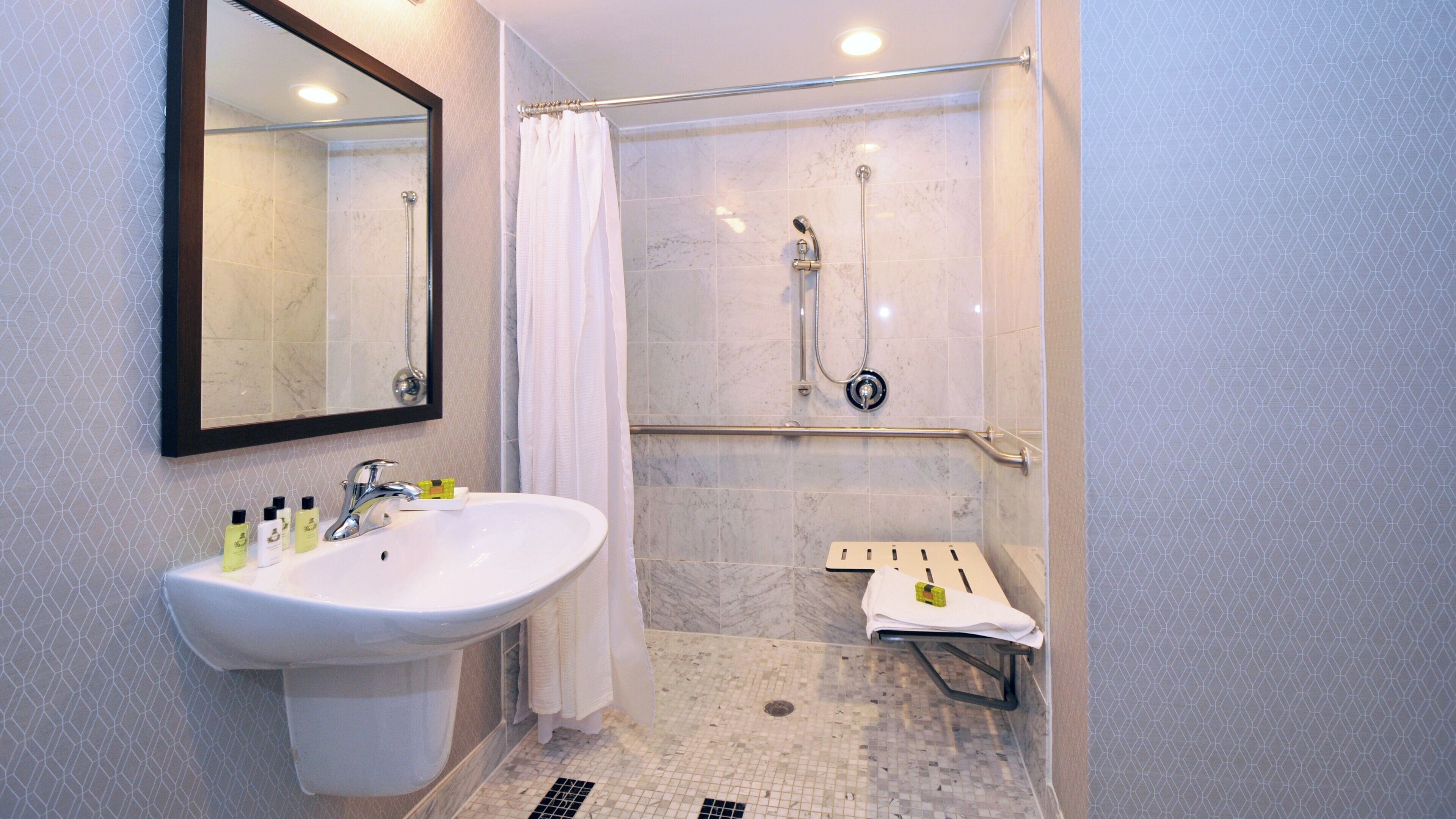 A bathroom with a sink, mirror, shower, and towel rack.
