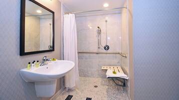 A bathroom with a sink, mirror, shower, and towel rack.