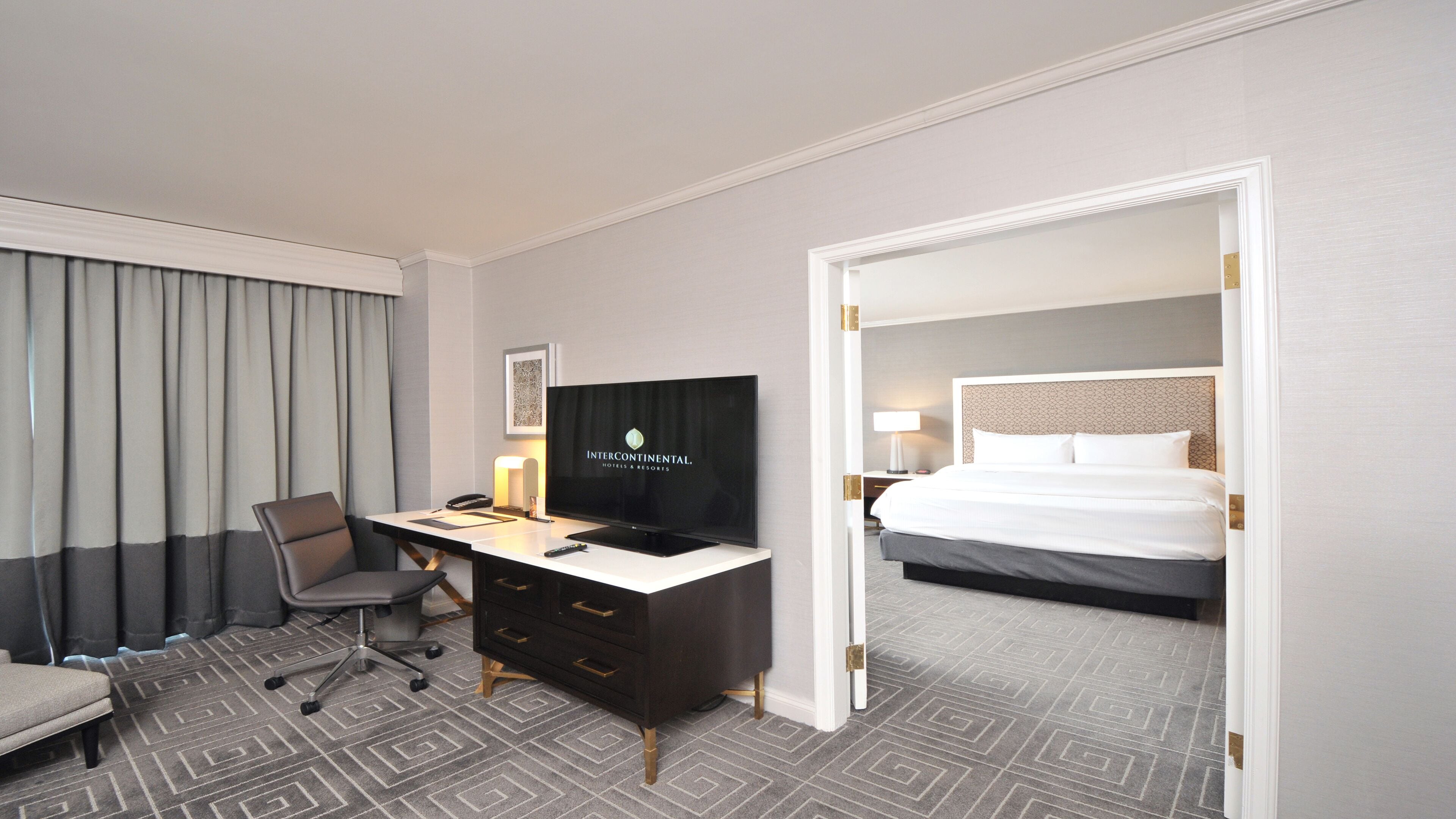 A hotel room with a desk, chair, television, and a bed.