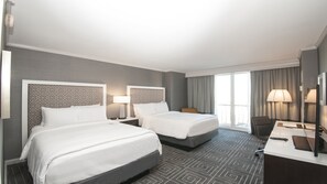 Ein Hotelzimmer mit zwei Betten, einem Schreibtisch, einem Stuhl und einem großen Fenster mit Vorhängen.