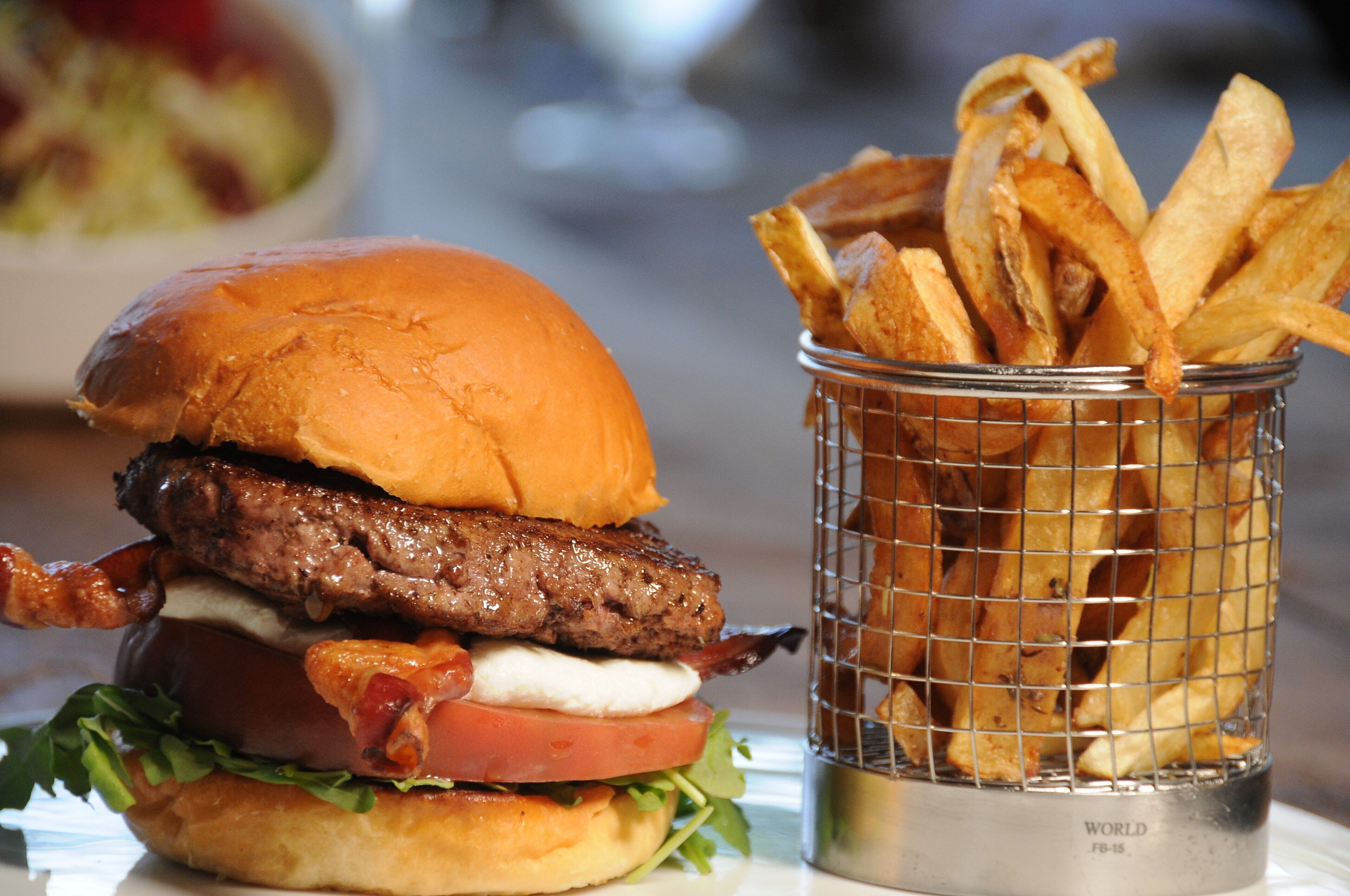 A burger with a beef patty, bacon, lettuce, tomato, and cheese, alongside a basket of fries.