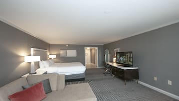 Quarto de hotel com cama, escrivaninha com televisão, sofá e poltrona.