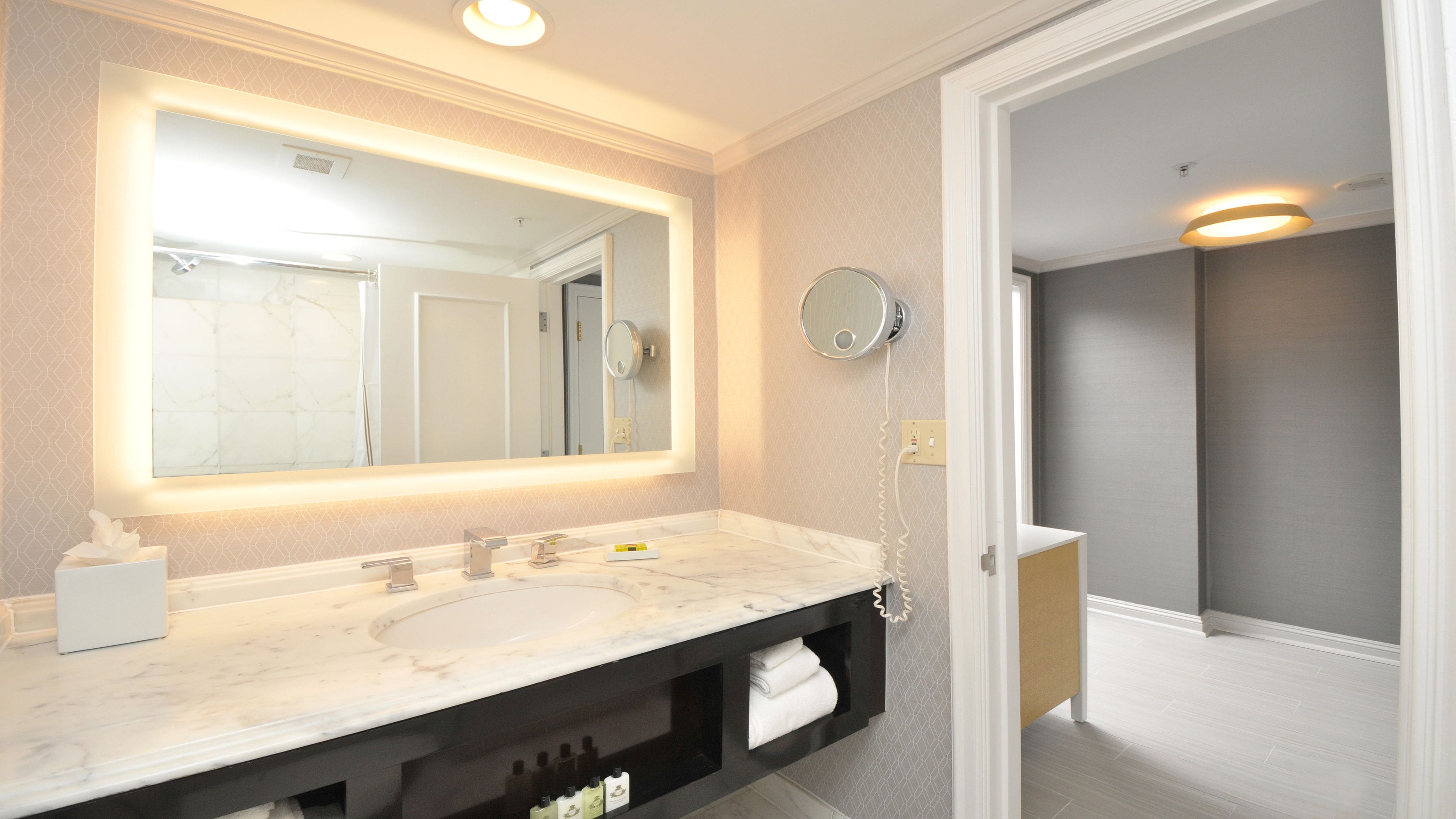 A modern bathroom with a large mirror, two sinks, and a vanity with storage.