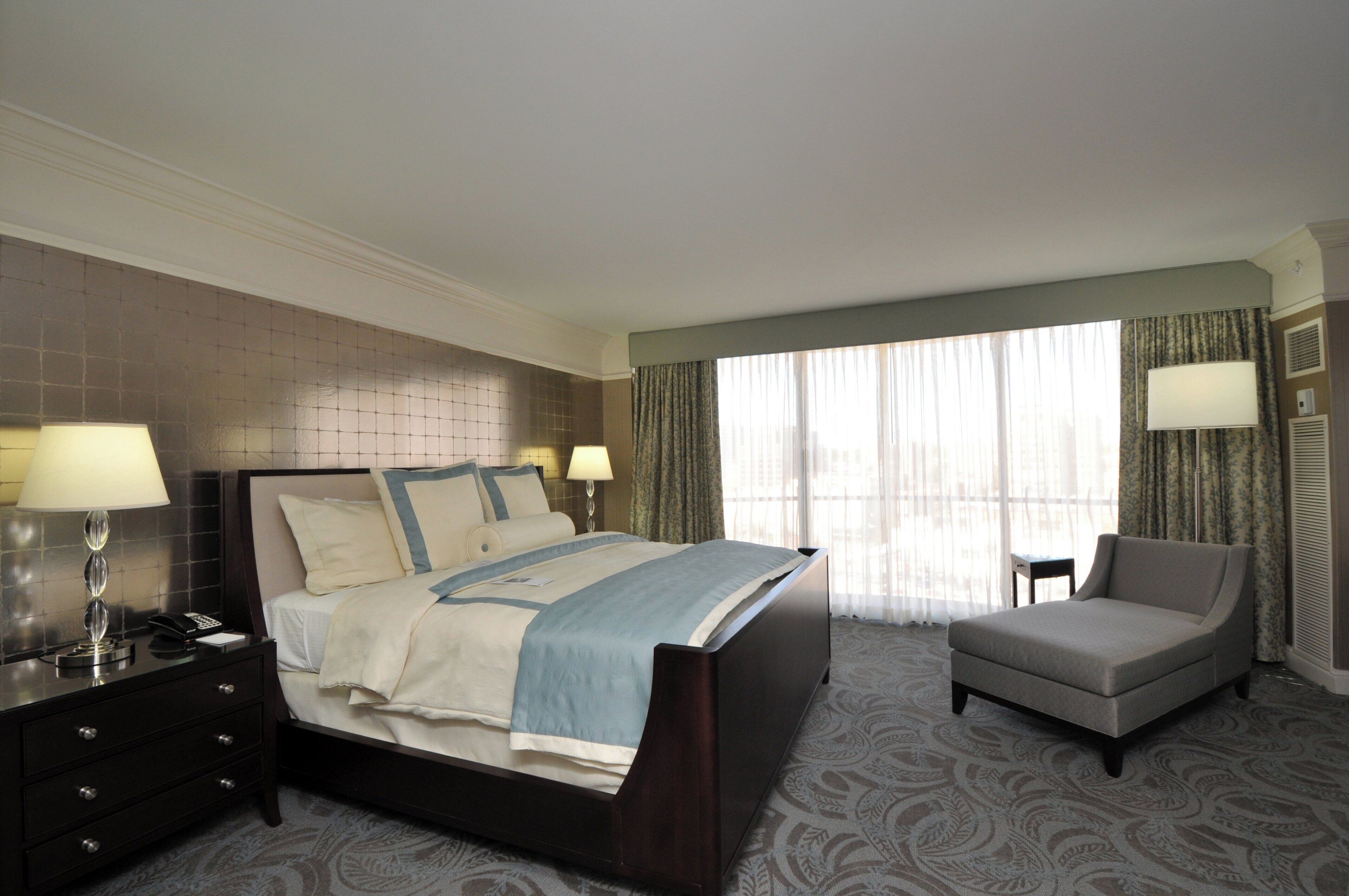 A hotel room with a bed, bedside tables, a chair, and a window with curtains.