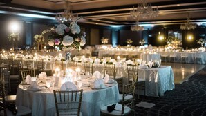 Un salón de banquetes con mesas redondas, manteles blancos y centros de mesa florales.