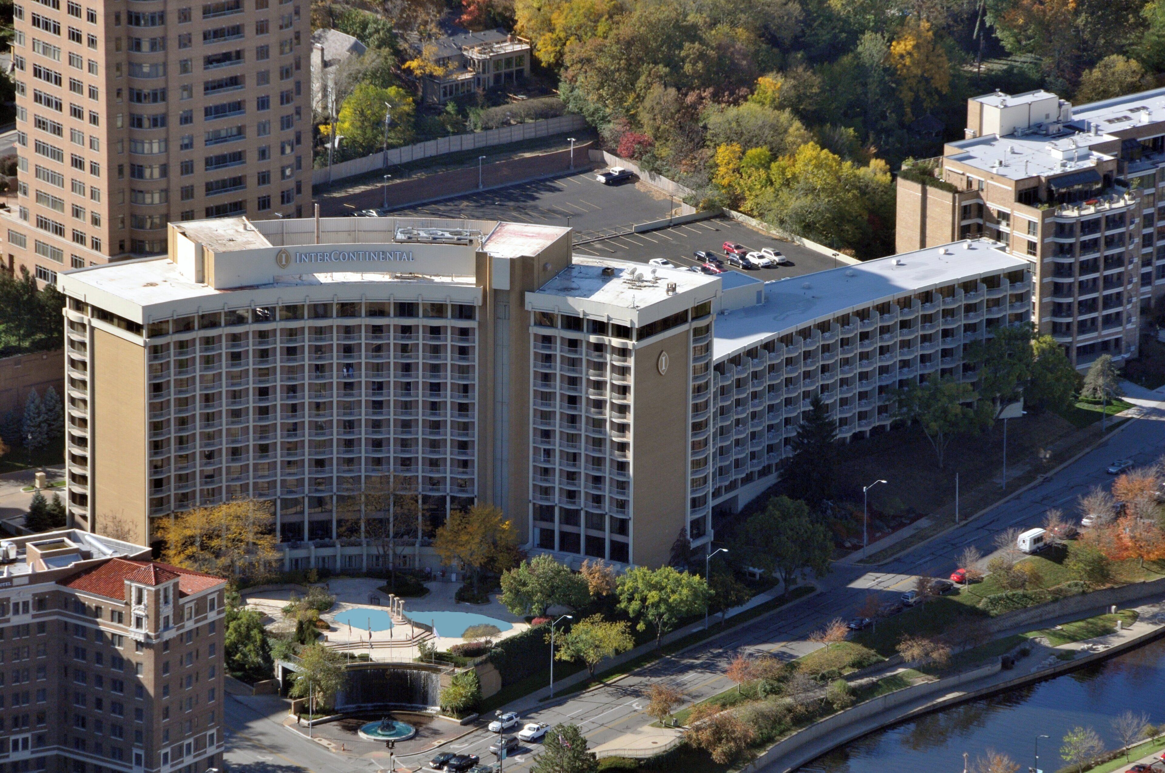 A multi-story hotel with a central courtyard, parking area, and a swimming pool.