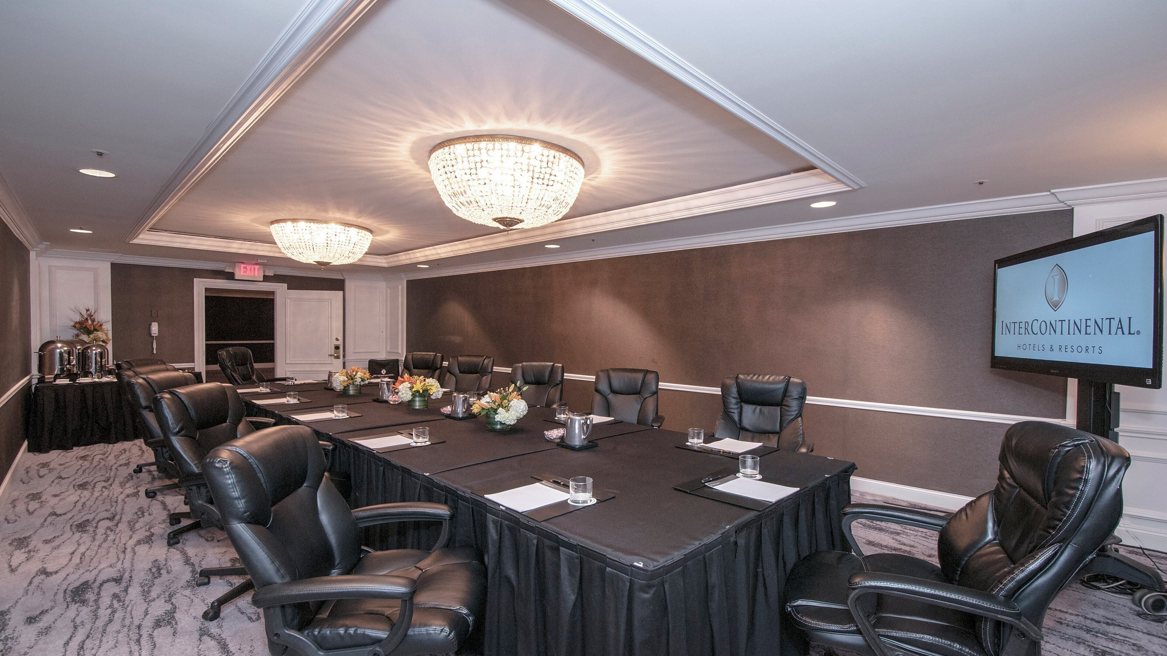 A conference room with a long table, leather chairs, a chandelier, and a screen displaying the Intercontinental Hotels & Resorts logo.